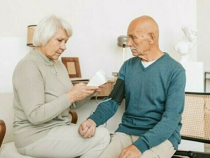 Frau misst Blutdruck eines älteren Mannes mit Alzheimer