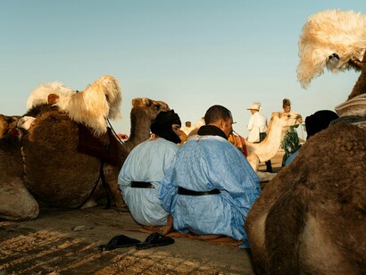 Nomadic people resting near camels in the desert, representing Morocco’s enduring tribal traditions