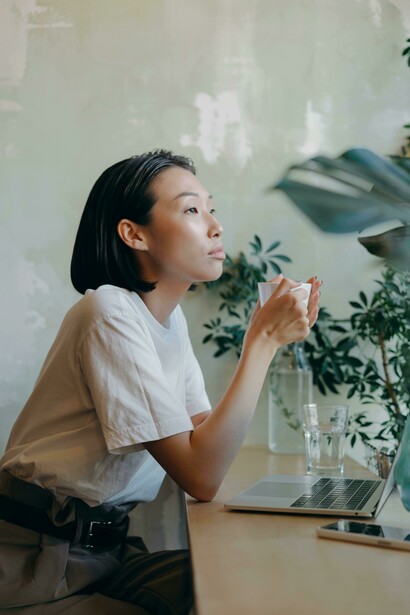 A woman in a white shirt sits on a chair in a café, speaking on the phone in solitude