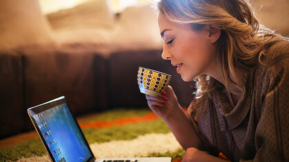 A blonde woman working on her laptop at home during sunset, immersed in writing as warm golden light fills the room