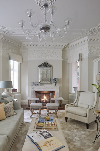 Serene living room featuring intricate plasterwork of its ceiling and cornice, a Venetian antique mirror, Italian marble fireplace, Murano glass chandeliers, and blue coral from Katharine Pooley’s boutique