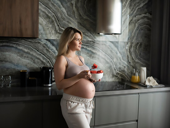 A medium shot of a pregnant woman enjoying a fruit bowl, emphasizing the benefits of nutritious food choices during pregnancy for both mother and baby