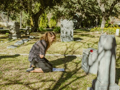 Uma mulher ajoelhada e chorando em um cemitério