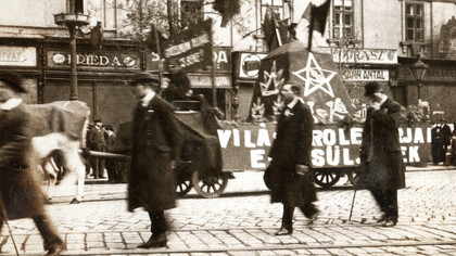 Cena de uma manifestação ou desfile ocorrido em 1º de maio de 1919 em Budapest, na rua Rákóczi, na antiga república soviética na Hungria. Na fotografia em preto e branco, pode-se observar signos políticos nas ruas