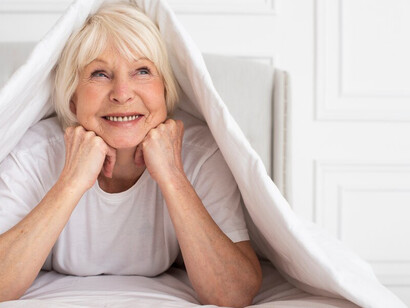 An elderly woman sitting comfortably under a blanket