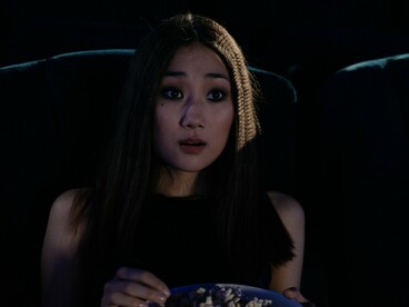 Uma espectadora segura um balde de pipoca e reage com surpresa enquanto assiste a um filme em uma sala escura. No cinema, as imagens e as histórias despertam emoções que nos aproximam de experiências humanas muito diferentes das nossas