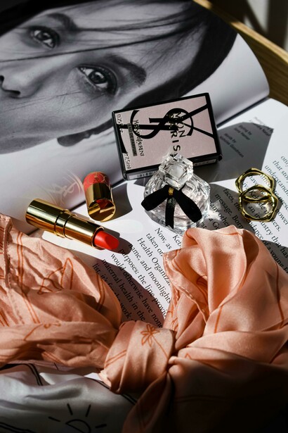 A bottle of perfume and a lipstick lie on top of a magazine
