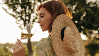 Stylish young girl with a foxy hairstyle donning a modern straw hat and trendy summer outfit poses elegantly with a glass of white wine amidst the picturesque vineyards of Hungary