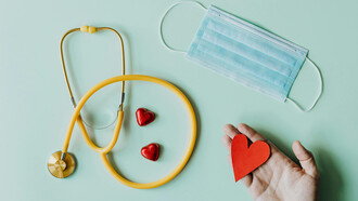 A stethoscope, a face mask and a hand holding a heart