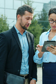 Business colleagues in business casual attire discuss work on a tablet outdoors