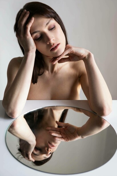 Primo piano di donna con gli occhi socchiusi, il cui viso è riflesso capovolto in uno specchio circolare