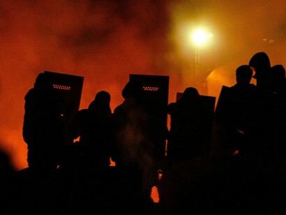 Blazing streets lit by orange and red flames as crowds gather, reflecting the combustible nature of civil unrest