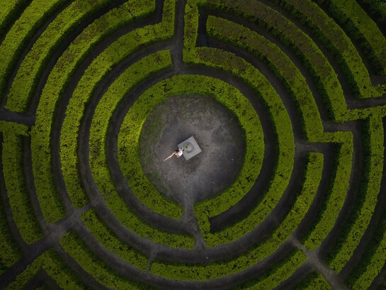 A person standing at the heart of a vast maze, symbolizing humanity’s struggle to maintain direction during times of uncertainty