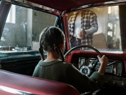 Sentada no banco do motorista, a menina brinca de conduzir como quem ensaia os caminhos da vida adulta sem ainda conhecer o peso das estradas