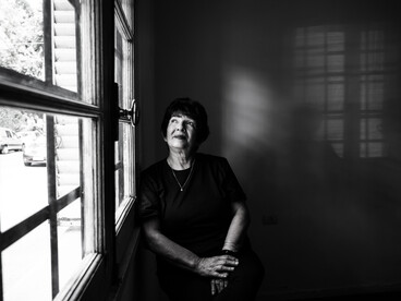 Black-and-white portrait of an elderly woman mourning a loved one while gazing through a window in reflective silence