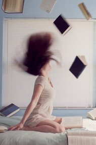 Woman sitting on bed with flying books