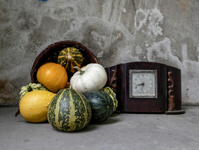 Different types of gourds and pumpkins on a concrete floor next to a wooden clock