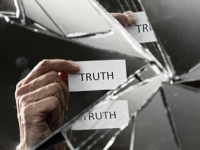 A shattered mirror reflecting fractured light as a hand holds a paper labelled “Truth,” reflecting the distortion of reality in modern media