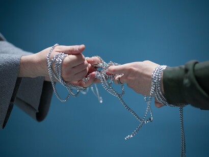 Fingers loosening their hold on intertwined chains, reflecting the choice to stop resisting what cannot be changed
