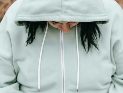 A woman who is an introvert is wearing her hoodie on her head and looking down