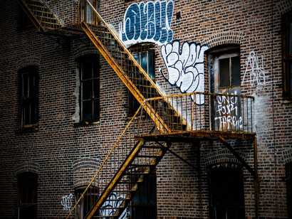 A view of a rundown brick building and its emergency exit stair, with some graffiti on it