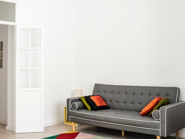 Uma sala ampla reúne sofá cinza, almofadas coloridas, tapetes de desenhos geométricos e um lustre de estilo clássico. A mistura de elementos evidencia como uma casa pode reunir diferentes referências e, ao mesmo tempo, tornar-se uma expressão da identidade de quem a habita