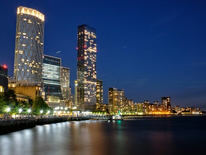 A scenic blue hour view of Rotterdam, showcasing a bridge over the waterfront with glowing city lights and contemporary architecture in the background