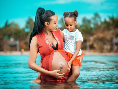 A pregnant African woman is holding her child in a river