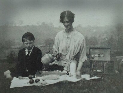 Mulher com seu filho em foto antiga. Ao tocar a hora congelada, sentiu o peso de tudo que havia evitado. As engrenagens estavam enferrujadas, cobertas de um pó fino, como memórias que ninguém quer reviver