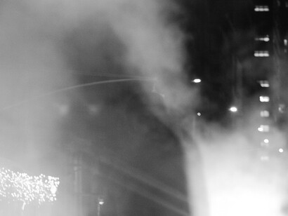 Una figura solitaria permanece entre el humo de una calle nocturna, rodeada por las luces difusas de la ciudad