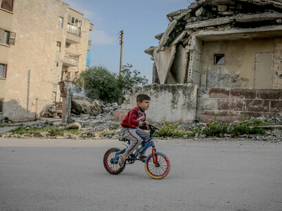 A child with a bicycle walks through a demolished city in Idlib, Idlib Governorate, Syria