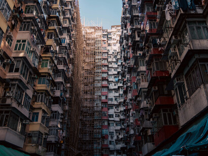 A low-angle perspective of high-rise housing in Hong Kong, reflecting the pressures of overcrowding, rising living costs, and urban poverty