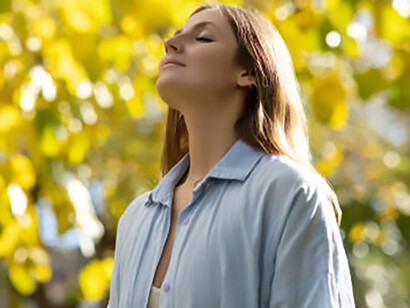 A woman with closed eyes and hands on her chest, practicing deep breathing amidst the calm of a forest