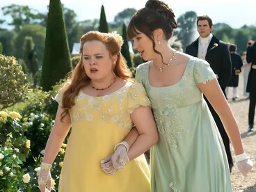Penelope Featherington and Eloise Bridgerton from Bridgerton walking through a garden in pastel embroidered dresses, representing the softer side of romantic Regency fashion