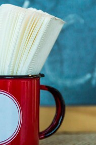 Guardanapos guardados numa caneca vermelha, à espera de uso como tantas presenças silenciosas que ocupam espaço na rotina sem realmente cumprir a função