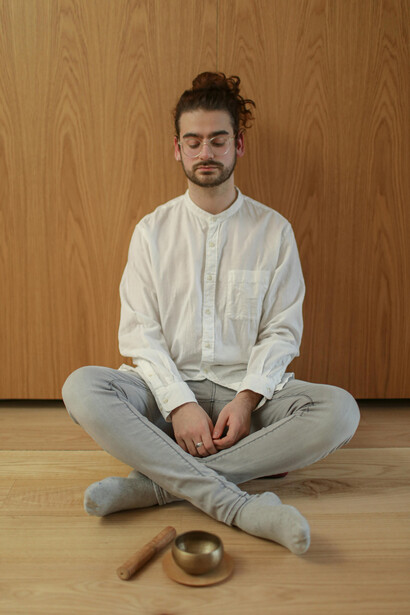 An adult man meditates indoors beside a candle and a singing bowl, creating a calm atmosphere focused on mindfulness, relaxation, and mental well-being