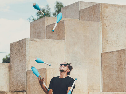 A man in sunglasses juggles five clubs