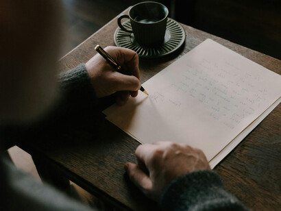 Hombre escribiendo en papel mientras bebe un té