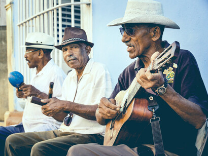 Three elderly Cuban men sit and play music together, singing