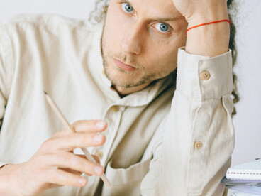 Young man showing signs of stress and emotional fatigue at work, surrounded by notes on his desk, reflecting workplace burnout and Gen-Z anxiety