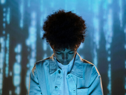 A boy using a mobile phone in front of flowing data, representing life in a data-driven world