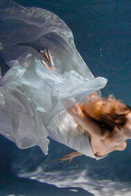 A graceful body suspended in water in a flowy white dress, conveying a weightless, unhurried state that mirrors emotional release