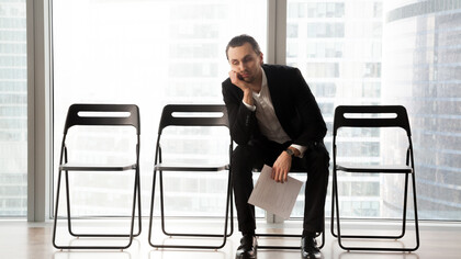 A bored young man in a suit sits in a waiting room for a job interview, looking upset