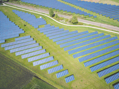 Aerial shot of a green field in Germany, featuring rows of blue solar panels, highlighting the integration of clean energy with nature