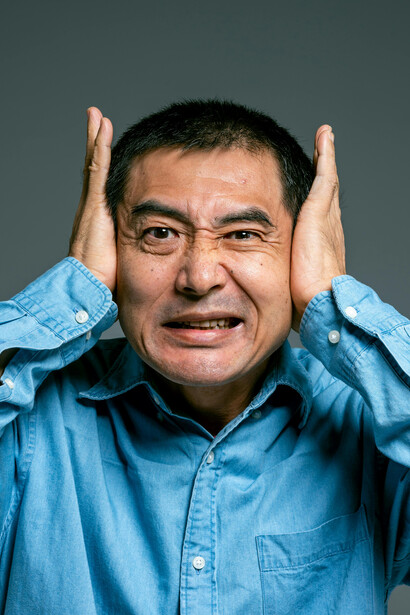 Wearing a blue denim button-up shirt, a man stands frozen in worry, anxiety written all over him