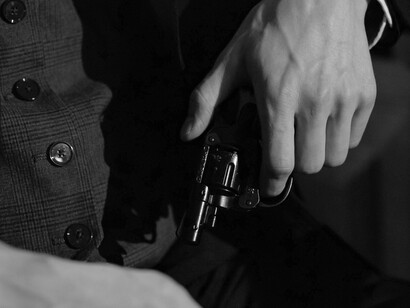 Bathed in dramatic lighting, a suited figure grips a pistol—an unsettling reminder of how crime stories turn criminals into legends