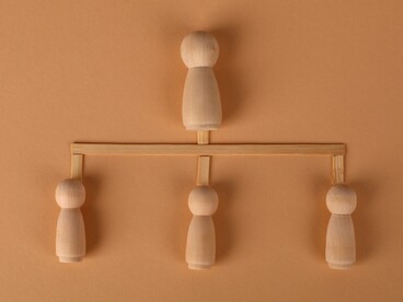 A group of wooden figures positioned beneath one figure at the highest level, symbolizing the structure of leadership and obedience in the workplace