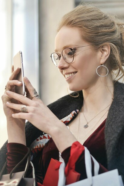 A woman checking her phone and carrying shopping bags, probably looking for a product seen online 