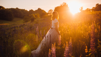 A woman in a bright dress walks across a field in the glow of sunset