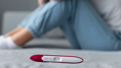 A woman sitting on the floor, appearing invisible and distressed behind a negative pregnancy test, reflecting the emotional impact of infertility